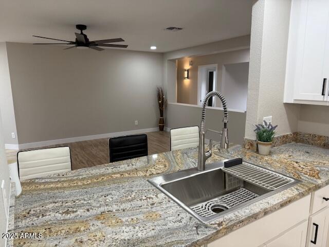 kitchen with wood finished floors, a sink, white cabinetry, light stone countertops, and ceiling fan