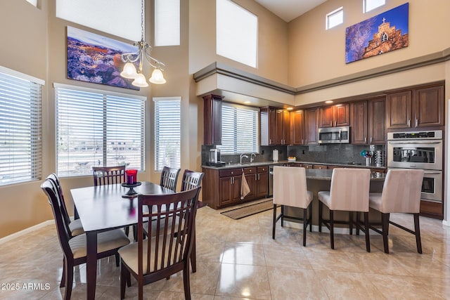 tiled dining room featuring sink, a wealth of natural light, a chandelier, and a high ceiling