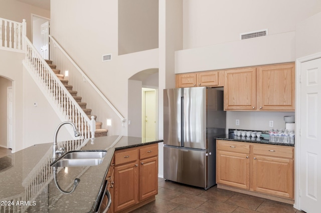 kitchen featuring sink, stainless steel appliances, dark tile patterned floors, a towering ceiling, and dark stone counters