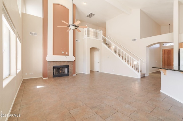 unfurnished living room with a tile fireplace, ceiling fan, beamed ceiling, high vaulted ceiling, and light tile patterned floors