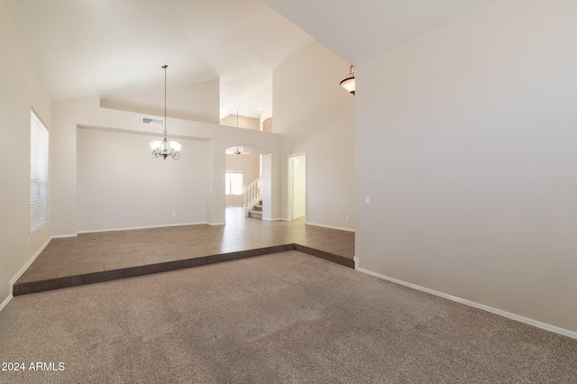 unfurnished living room with carpet, high vaulted ceiling, and a chandelier