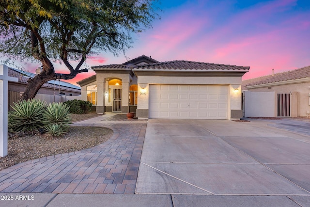 mediterranean / spanish-style home featuring concrete driveway, a tiled roof, an attached garage, fence, and stucco siding