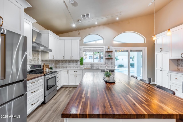 kitchen with a kitchen island, appliances with stainless steel finishes, wall chimney range hood, white cabinetry, and wooden counters