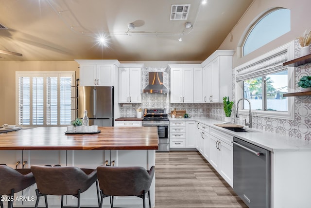 kitchen with stainless steel appliances, wall chimney range hood, a sink, and white cabinets