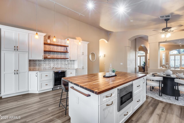 kitchen with open shelves, wine cooler, stainless steel microwave, white cabinetry, and wooden counters