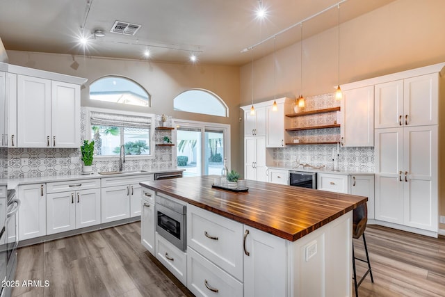 kitchen with butcher block counters, stainless steel appliances, white cabinetry, open shelves, and a sink