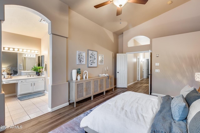 bedroom with arched walkways, ensuite bathroom, light tile patterned flooring, a sink, and baseboards