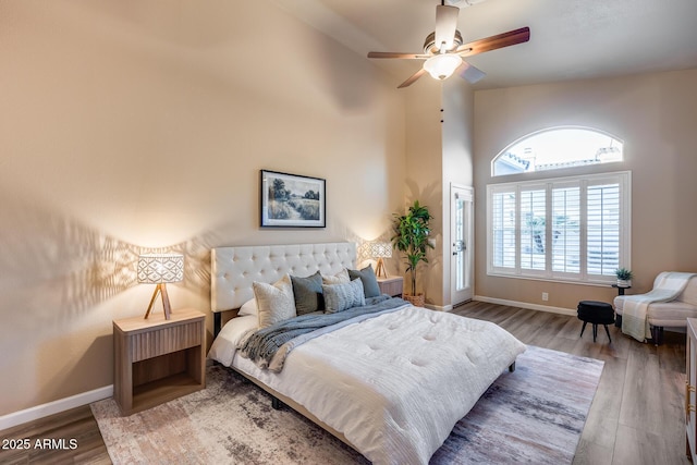 bedroom featuring ceiling fan, a high ceiling, baseboards, and wood finished floors