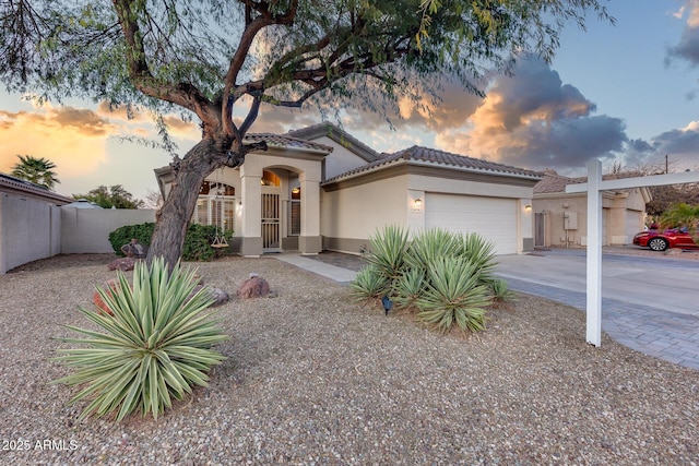 mediterranean / spanish-style house with stucco siding, an attached garage, fence, driveway, and a tiled roof