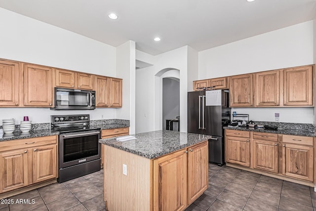 26264 N 74th Ln, Peoria, AZ 85383 - kitchen featuring appliances with stainless steel finishes, arched walkways, dark tile patterned floors, a center island, and dark stone counters