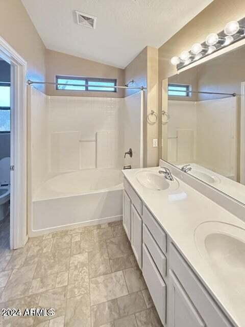 bathroom with shower / bath combination, a textured ceiling, vaulted ceiling, and vanity