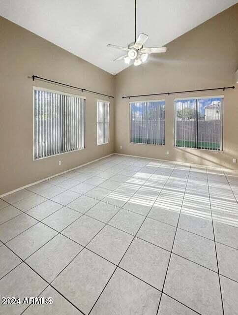 tiled empty room with ceiling fan, a wealth of natural light, and lofted ceiling