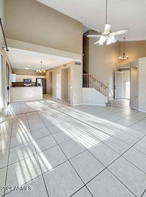 unfurnished living room with light tile patterned floors, ceiling fan with notable chandelier, and high vaulted ceiling