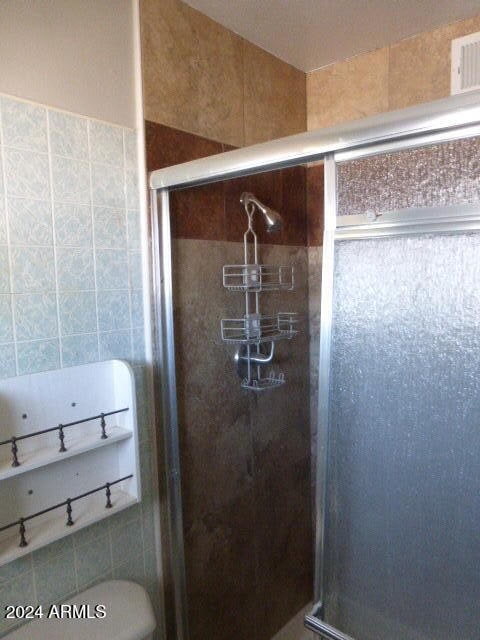 bathroom with a shower with shower door, tile walls, and toilet