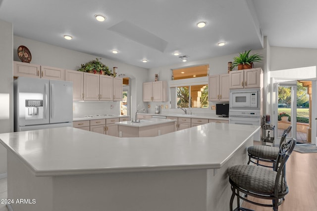 kitchen featuring a breakfast bar, white appliances, lofted ceiling, a spacious island, and light hardwood / wood-style flooring