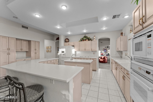 kitchen with a breakfast bar, white appliances, sink, light tile patterned floors, and an island with sink