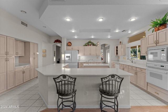 kitchen featuring white appliances, a kitchen island with sink, sink, light tile patterned floors, and a kitchen bar