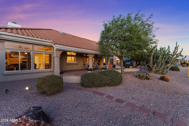 back house at dusk featuring a patio area