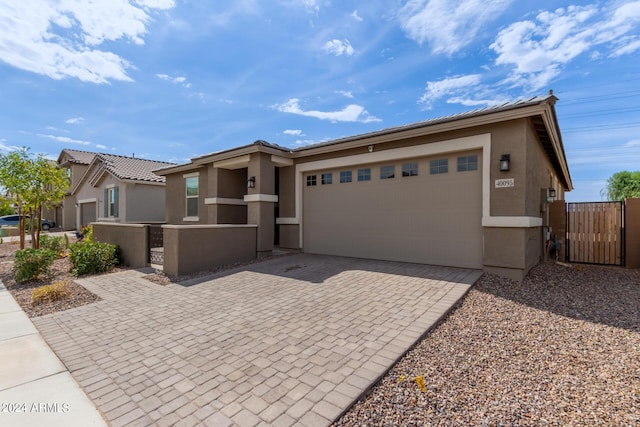 view of front facade featuring fence, stucco siding, decorative driveway, an attached garage, and a gate