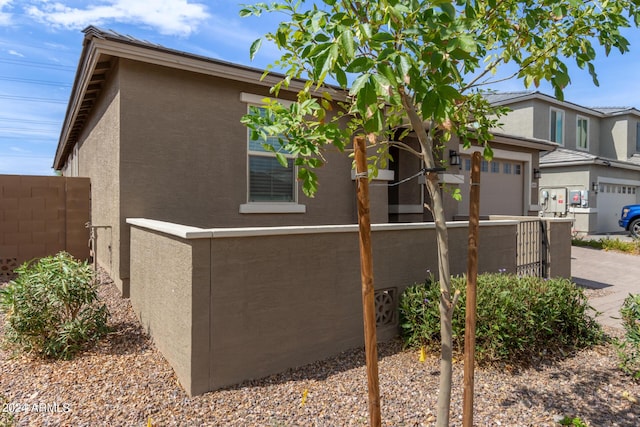 view of side of property with stucco siding, a garage, driveway, and fence