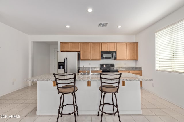 kitchen featuring light tile patterned flooring, a breakfast bar area, black appliances, and an island with sink