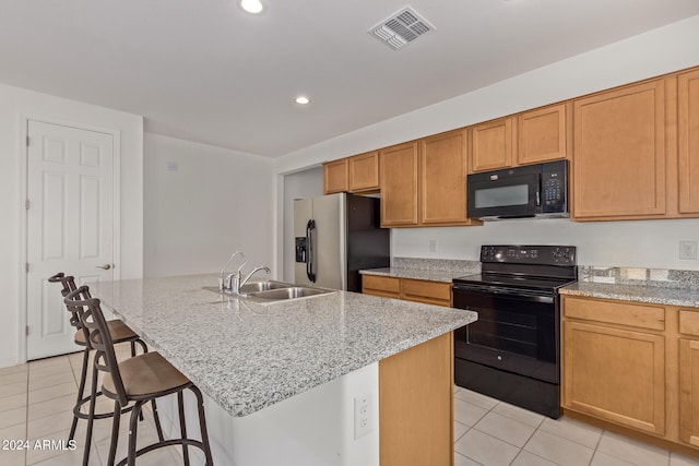 kitchen with light tile patterned flooring, black appliances, an island with sink, sink, and light stone countertops