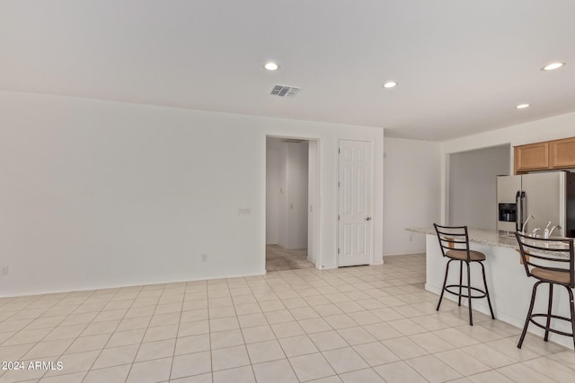 kitchen featuring a breakfast bar, stainless steel refrigerator with ice dispenser, light tile patterned floors, and light stone countertops