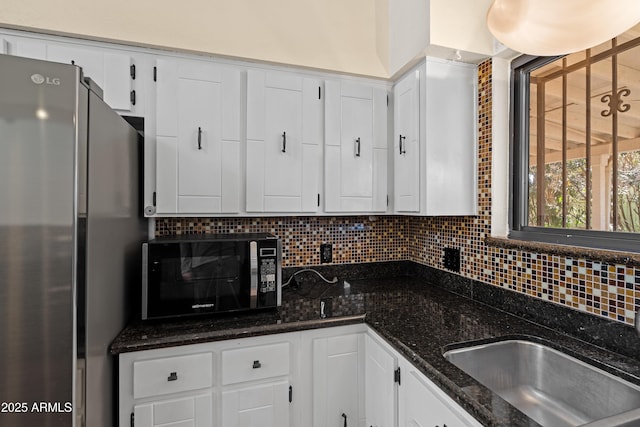 kitchen with tasteful backsplash, dark stone countertops, stainless steel refrigerator, and white cabinets