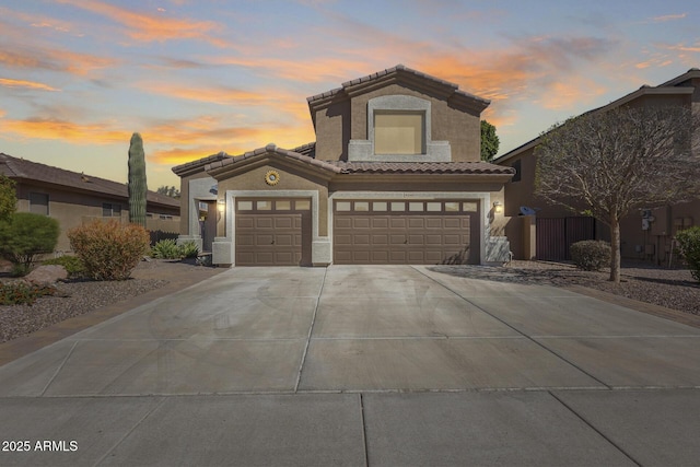mediterranean / spanish-style home featuring a tile roof, stucco siding, fence, an attached garage, and driveway