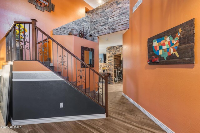 stairway with baseboards, visible vents, wood finished floors, and a towering ceiling