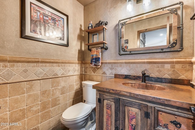 bathroom featuring tile walls, toilet, vanity, wainscoting, and a textured wall