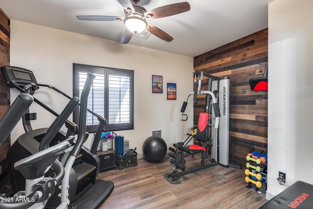 exercise room with wood finished floors, wood walls, and ceiling fan
