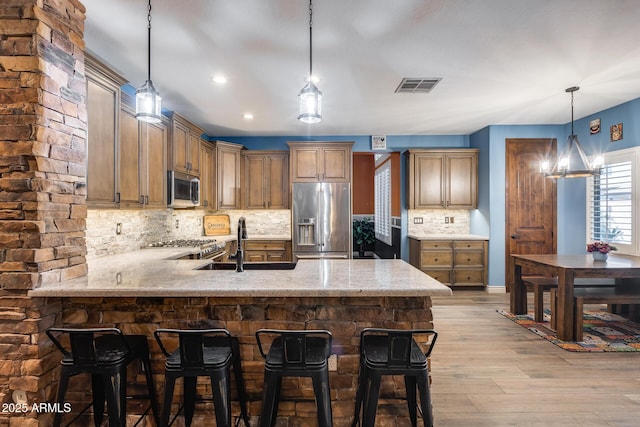 kitchen with tasteful backsplash, light wood-type flooring, stainless steel appliances, visible vents, and a peninsula