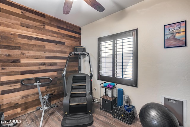 exercise area with a ceiling fan, wood finish floors, and wooden walls