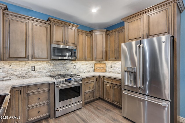 kitchen with wood finished floors, stainless steel appliances, backsplash, light stone countertops, and brown cabinets