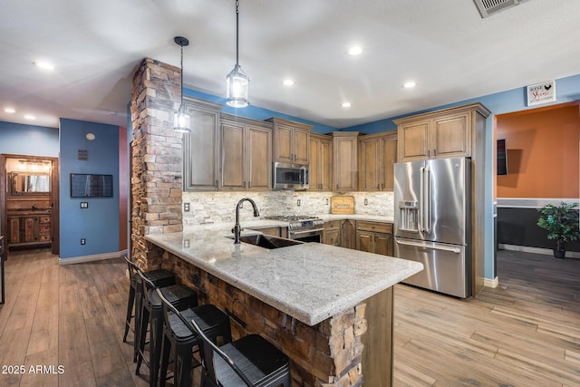 kitchen featuring a sink, a kitchen bar, premium appliances, a peninsula, and decorative backsplash
