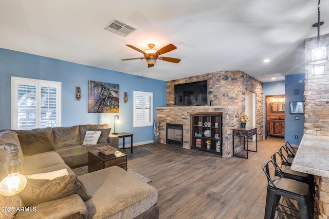 living area with baseboards, visible vents, a stone fireplace, ceiling fan, and wood finished floors