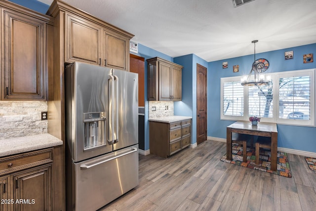 kitchen with baseboards, wood finished floors, stainless steel fridge with ice dispenser, an inviting chandelier, and backsplash