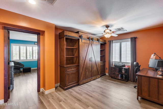 office space with baseboards, a barn door, light wood finished floors, visible vents, and ceiling fan