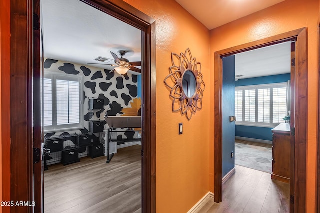hall with baseboards, visible vents, wood finished floors, and a textured wall