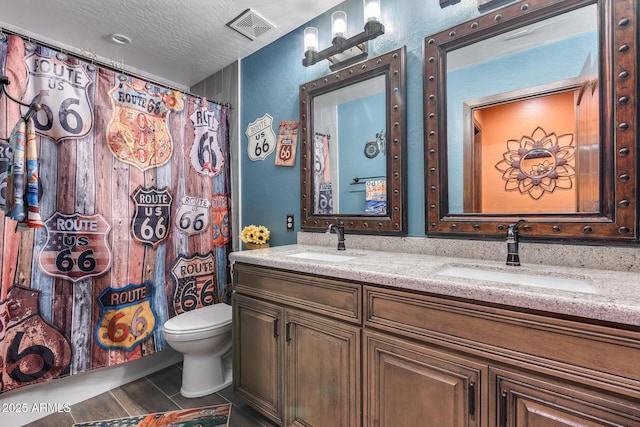 full bath featuring double vanity, visible vents, toilet, and a sink