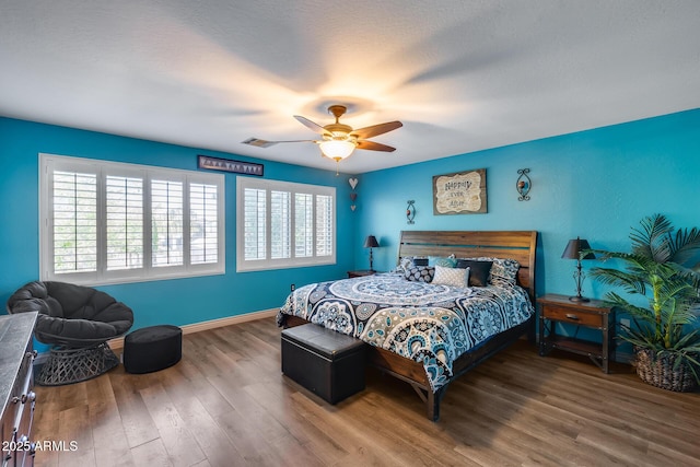 bedroom with a textured ceiling, visible vents, baseboards, ceiling fan, and wood finished floors