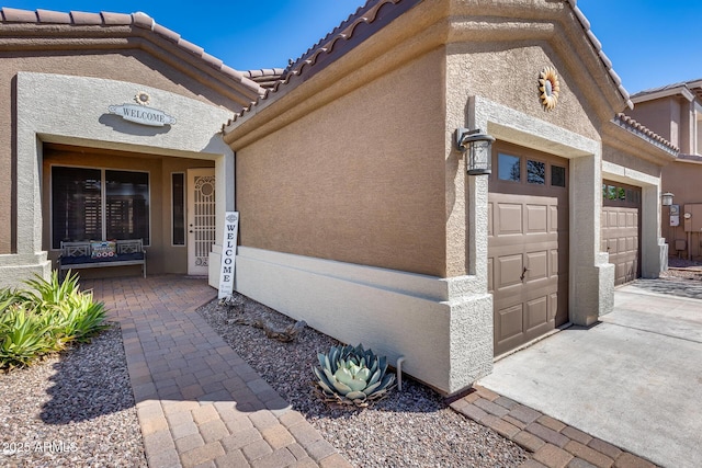 view of exterior entry with a tile roof, stucco siding, and an attached garage