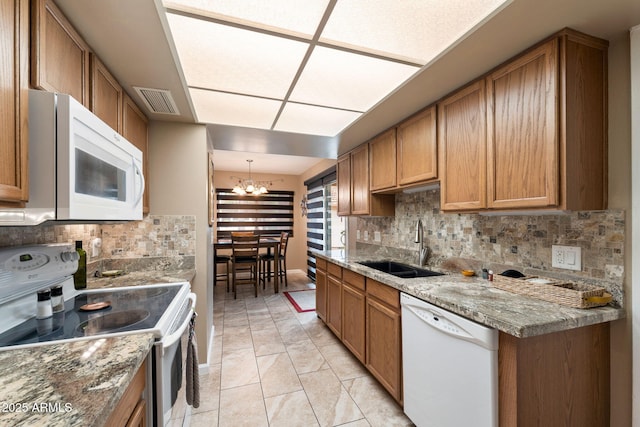 kitchen with tasteful backsplash, white appliances, sink, light tile patterned floors, and a notable chandelier