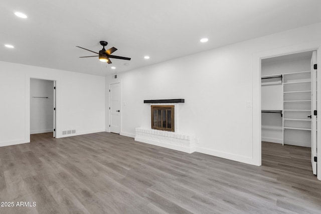 unfurnished living room with ceiling fan, a fireplace, and wood-type flooring