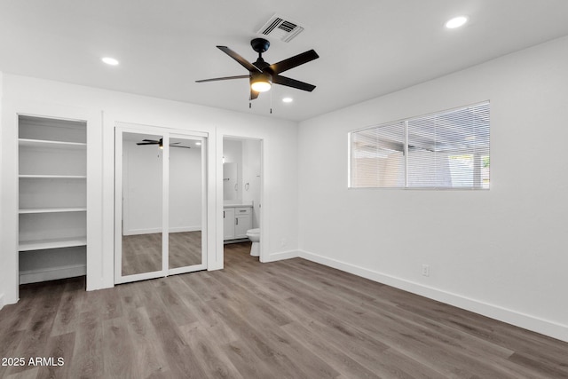 unfurnished bedroom featuring ceiling fan, hardwood / wood-style flooring, ensuite bath, and multiple closets