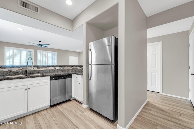 kitchen with sink, appliances with stainless steel finishes, white cabinetry, light hardwood / wood-style floors, and dark stone counters