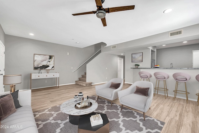 living room featuring bar, ceiling fan, and light wood-type flooring