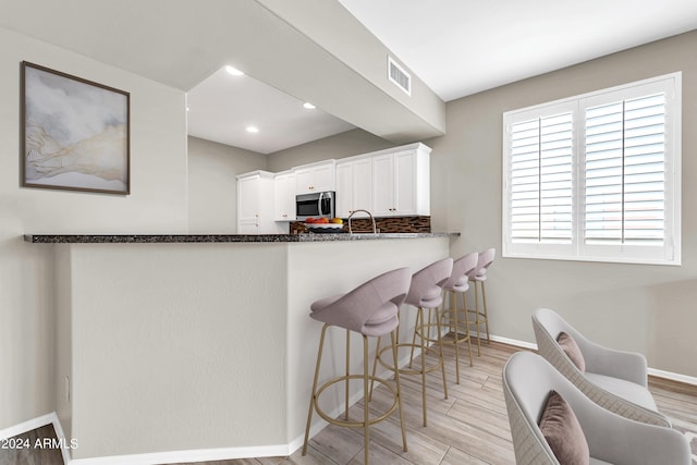 kitchen featuring tasteful backsplash, kitchen peninsula, white cabinets, and light wood-type flooring