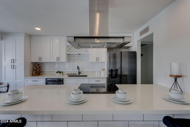 kitchen featuring white cabinets, stainless steel fridge, wall chimney range hood, and sink